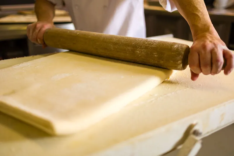 Un pastisser estira la massa de full amb un corró de fusta